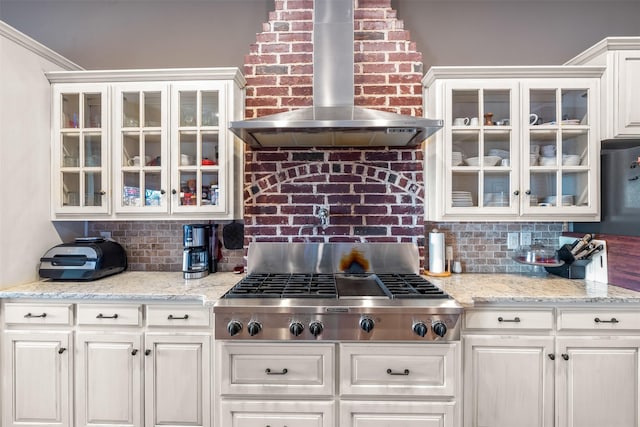 kitchen with wall chimney exhaust hood, stainless steel gas stovetop, white cabinets, and backsplash