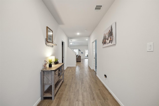 corridor with visible vents, light wood-style flooring, and baseboards