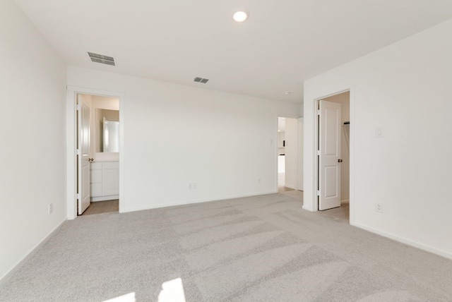 unfurnished bedroom featuring baseboards, visible vents, ensuite bathroom, and light colored carpet