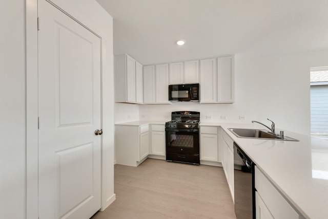 kitchen with a sink, white cabinets, light countertops, black appliances, and light wood finished floors