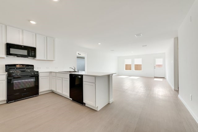 kitchen featuring open floor plan, white cabinetry, a sink, a peninsula, and black appliances