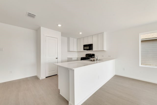 kitchen with light countertops, visible vents, light wood-style floors, a peninsula, and black appliances