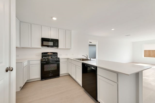 kitchen featuring light countertops, light wood-style flooring, a sink, a peninsula, and black appliances