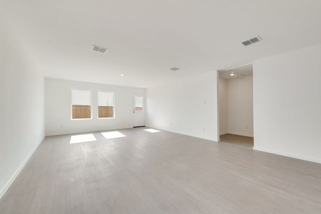 empty room featuring attic access, visible vents, baseboards, and wood finished floors