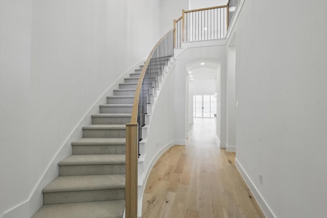 stairway featuring arched walkways, baseboards, a high ceiling, and wood finished floors