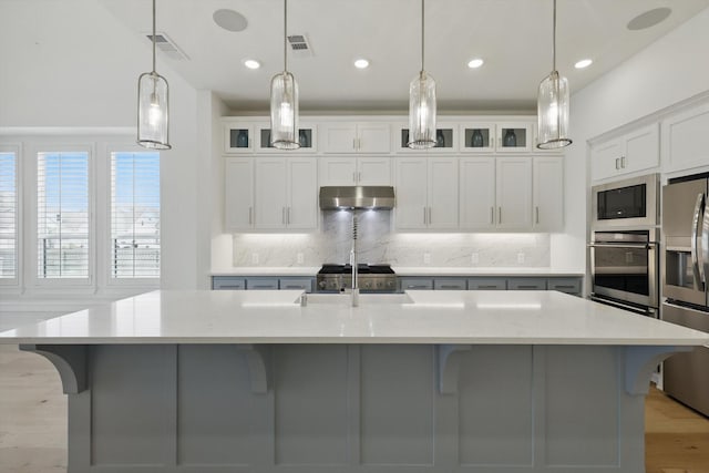 kitchen with under cabinet range hood, stainless steel appliances, a sink, visible vents, and backsplash