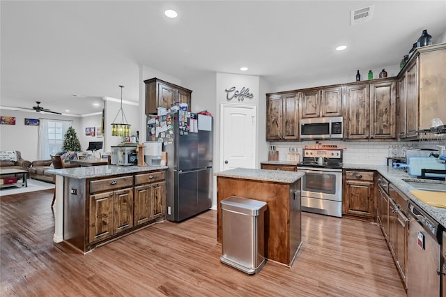 kitchen featuring decorative backsplash, light wood-style flooring, appliances with stainless steel finishes, open floor plan, and a center island