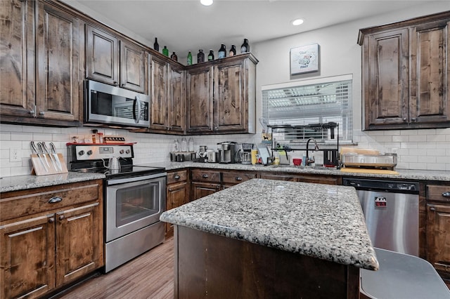 kitchen featuring stainless steel appliances, a sink, decorative backsplash, and light stone counters