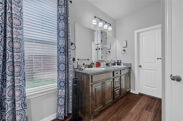 full bathroom with double vanity, baseboards, a sink, and wood finished floors