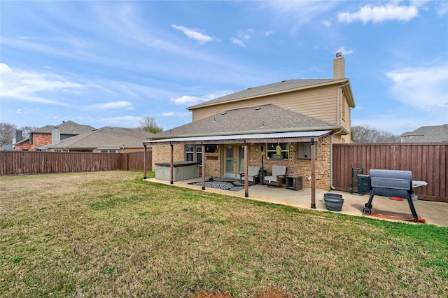 rear view of house featuring brick siding, a lawn, a hot tub, a patio area, and a fenced backyard