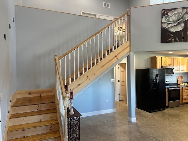 stairway with finished concrete flooring, baseboards, a high ceiling, and visible vents