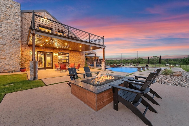 patio terrace at dusk with french doors, a water view, a balcony, an outdoor pool, and a fire pit