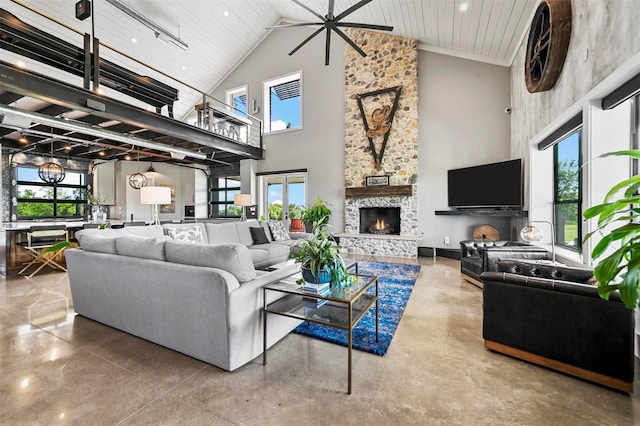 living area with a healthy amount of sunlight, high vaulted ceiling, concrete flooring, and a stone fireplace