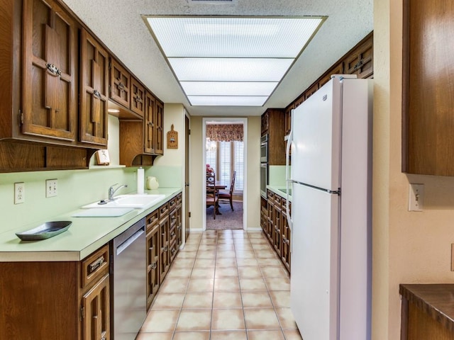 kitchen featuring light tile patterned floors, a sink, light countertops, stainless steel dishwasher, and freestanding refrigerator