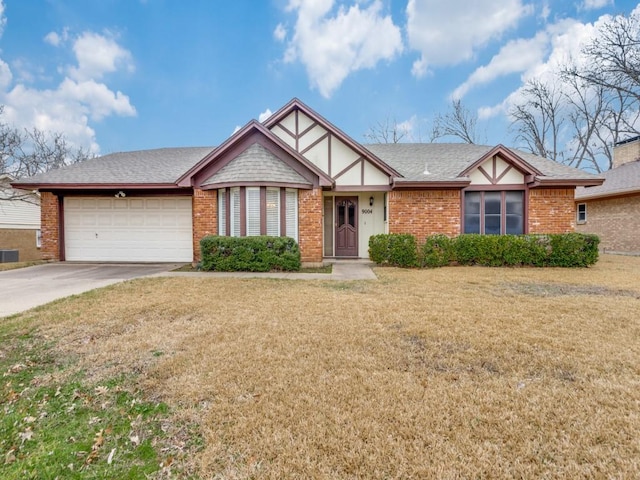 english style home featuring driveway, roof with shingles, an attached garage, a front yard, and brick siding