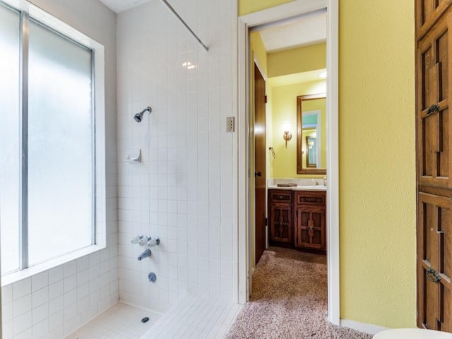 full bathroom featuring tiled shower, a textured wall, and vanity