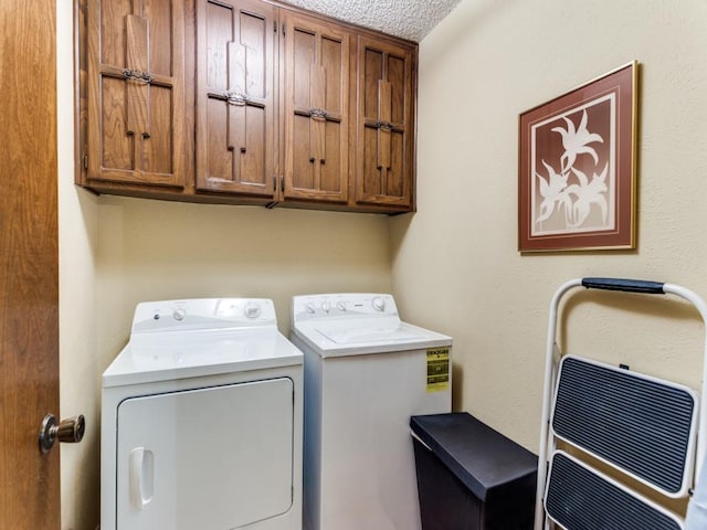 clothes washing area with a textured ceiling, washer and clothes dryer, and cabinet space