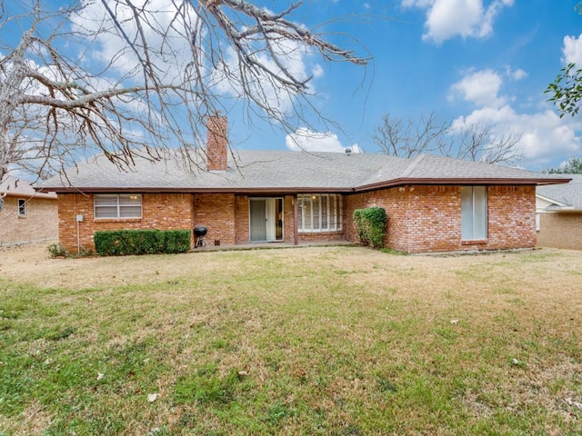 view of front of property featuring a front lawn, a chimney, a shingled roof, and brick siding