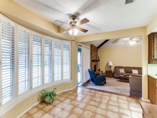 living area featuring visible vents, baseboards, ceiling fan, a textured ceiling, and a brick fireplace