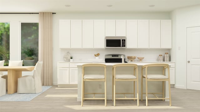 kitchen featuring light wood finished floors, stainless steel microwave, range, and white cabinets