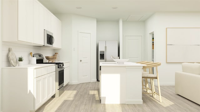 kitchen featuring a center island, light wood finished floors, stainless steel appliances, white cabinetry, and a kitchen bar