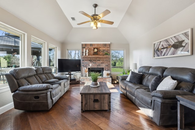 living area with visible vents, dark wood-type flooring, ceiling fan, vaulted ceiling, and a fireplace