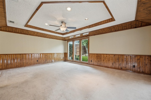 carpeted spare room with a tray ceiling, a textured ceiling, and wainscoting