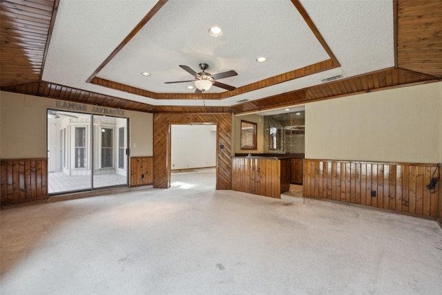 unfurnished living room featuring carpet floors, a raised ceiling, visible vents, wood walls, and ceiling fan