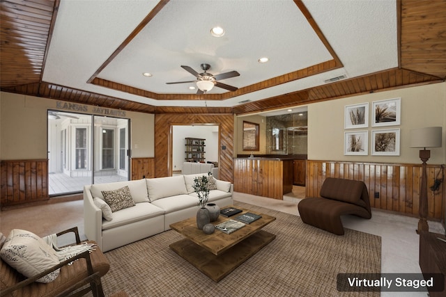 carpeted living room with a wainscoted wall, a tray ceiling, visible vents, and wooden walls