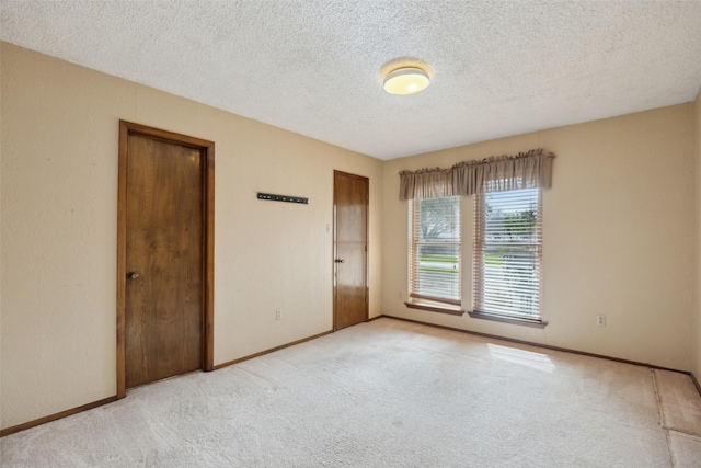 spare room with a textured ceiling, carpet, and baseboards