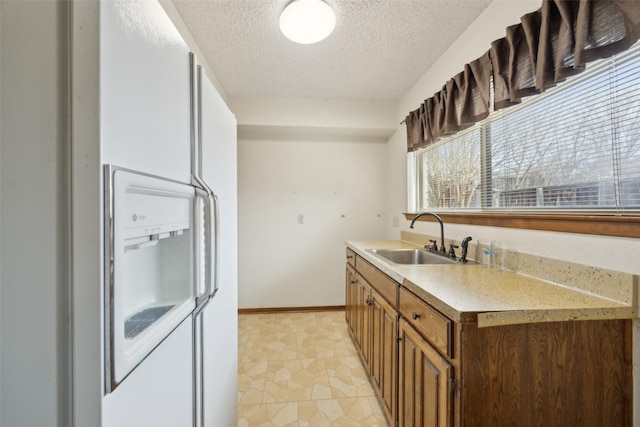 kitchen with white refrigerator with ice dispenser, baseboards, light countertops, a textured ceiling, and a sink