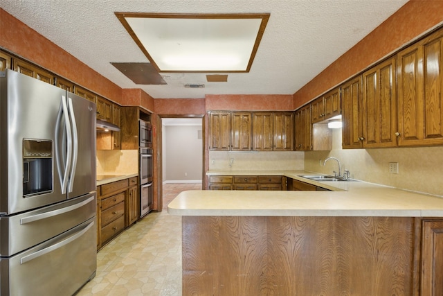 kitchen featuring stainless steel appliances, a peninsula, a sink, and light countertops