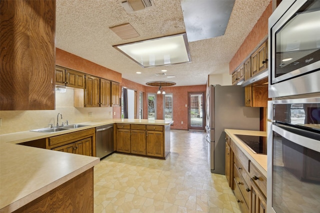 kitchen featuring a peninsula, a sink, visible vents, appliances with stainless steel finishes, and brown cabinetry