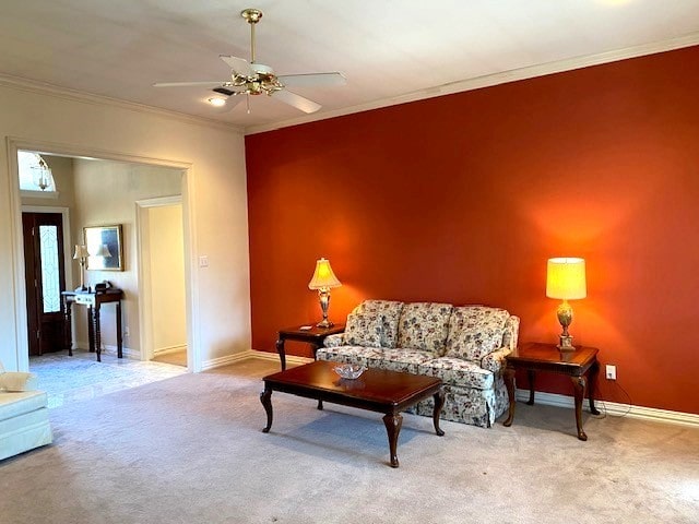 carpeted living area featuring a ceiling fan, baseboards, and crown molding