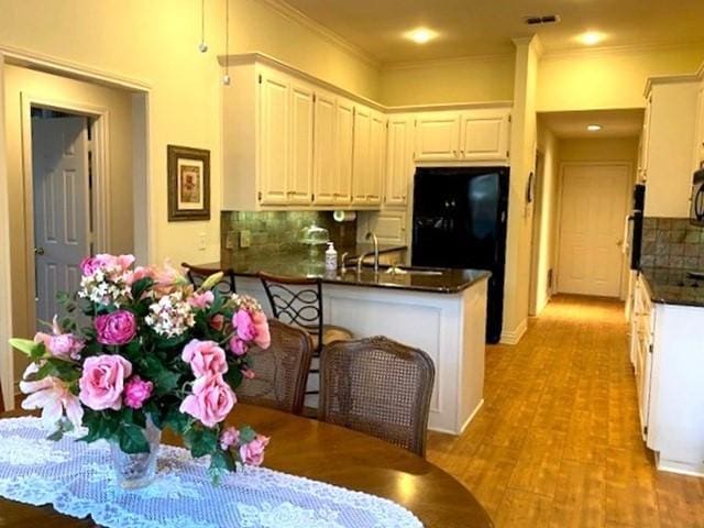 kitchen featuring tasteful backsplash, dark countertops, a peninsula, crown molding, and light wood-type flooring