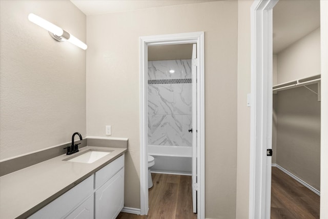 bathroom featuring bathtub / shower combination, toilet, wood finished floors, vanity, and a spacious closet