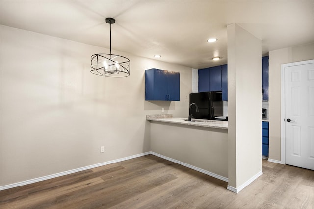 kitchen featuring baseboards, wood finished floors, freestanding refrigerator, blue cabinets, and light countertops