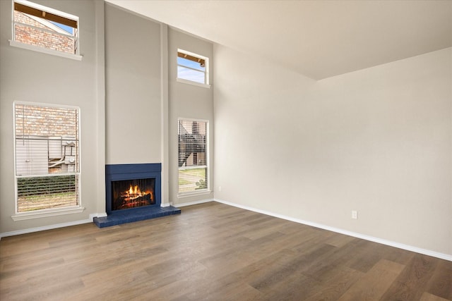 unfurnished living room with a lit fireplace, wood finished floors, and baseboards