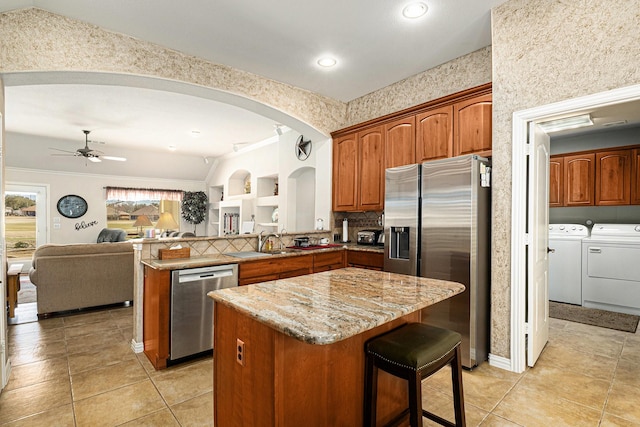 kitchen featuring light stone counters, a center island, appliances with stainless steel finishes, a sink, and separate washer and dryer