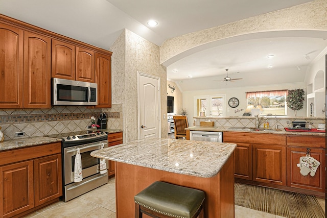 kitchen featuring appliances with stainless steel finishes, light stone counters, a sink, and a center island