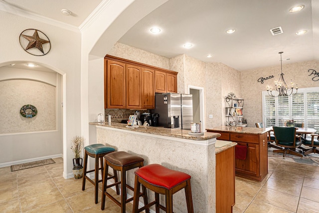 kitchen with a breakfast bar, brown cabinets, visible vents, stainless steel fridge, and a peninsula