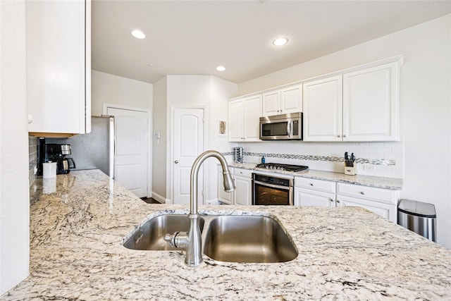 kitchen with appliances with stainless steel finishes, white cabinets, a sink, and light stone countertops