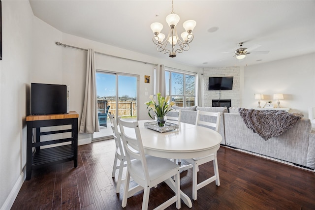 dining area featuring baseboards, a stone fireplace, hardwood / wood-style floors, and ceiling fan with notable chandelier