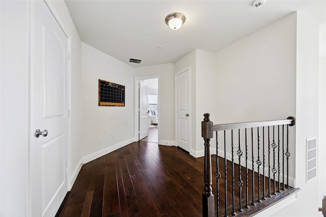 hall with hardwood / wood-style floors, an upstairs landing, visible vents, and baseboards