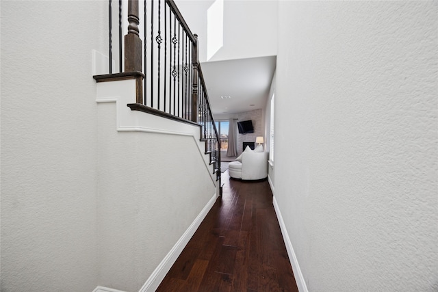 hallway with stairs, a textured wall, hardwood / wood-style floors, and baseboards