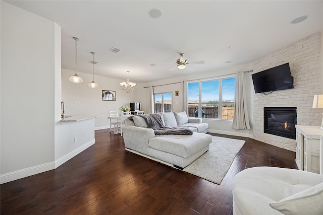 living room with ceiling fan with notable chandelier, a fireplace, visible vents, baseboards, and hardwood / wood-style floors