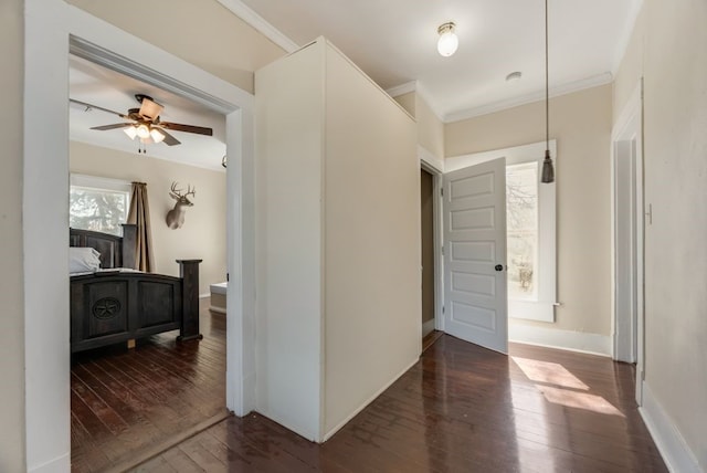 hallway with ornamental molding, dark wood-type flooring, and baseboards