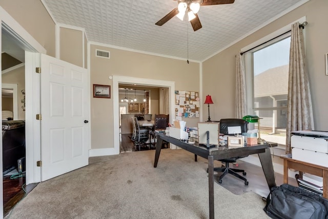 carpeted home office featuring baseboards, a ceiling fan, visible vents, and crown molding