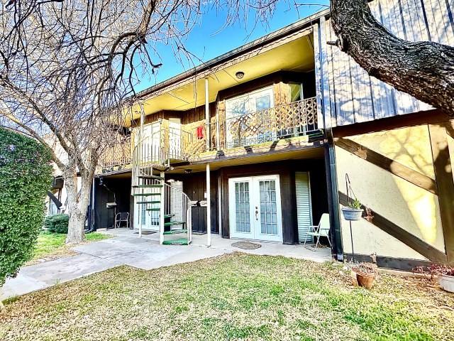 rear view of property featuring a yard, french doors, a patio, and a balcony