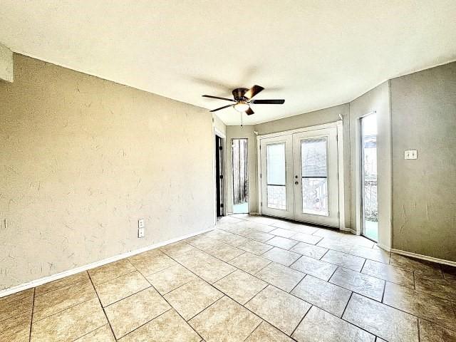 empty room featuring ceiling fan, a textured wall, french doors, and baseboards